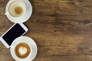 Kahve kalp desenli beyaz Kupası ve ahşap arka plan, üstten görünüm, iş online iş için fikirler akıllı telefon