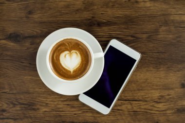 Kahve kalp desenli beyaz Kupası ve ahşap arka plan, üstten görünüm, iş online iş için fikirler akıllı telefon