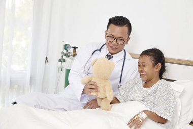 Tıbbi kavramı. Küçük kız ile bir oyuncak ayı tutan Doktor mutlu bir şekilde muayene olan hastanede gülümsüyor