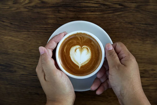 Hands holding coffee cup heart on coffee cup and woman nails on wood, valentine love concept.