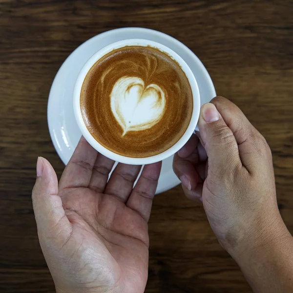 Hands holding coffee cup heart on coffee cup and woman nails on wood, valentine love concept.