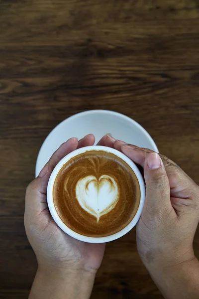 Hands holding coffee cup heart on coffee cup and woman nails on wood, valentine love concept.