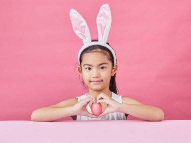 Mutlu küçük kız tavşan kulakları giyen ve pembe bir arka plan üzerinde renkli bir Easter egg gidiyor stüdyo çekim