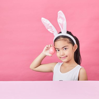 Mutlu küçük kız tavşan kulakları giyen ve pembe bir arka plan üzerinde renkli bir Easter egg gidiyor stüdyo çekim