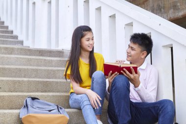 öğrenciler kitap kullanarak merdivenlerde oturan arkadaşlar