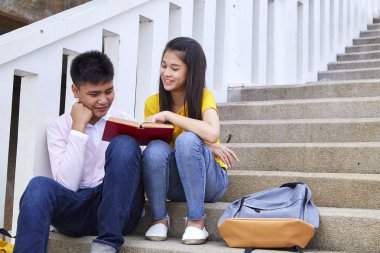 öğrenciler kitap kullanarak merdivenlerde oturan arkadaşlar