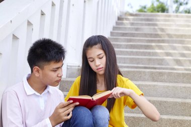 öğrenciler kitap kullanarak merdivenlerde oturan arkadaşlar