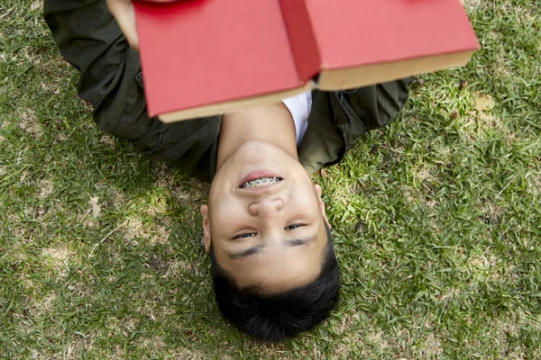Junge liegt und liest rotes Buch auf grünem Gras — Stockfoto