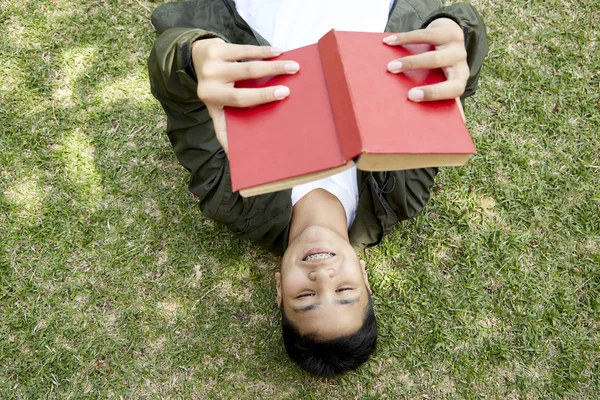 Junge liegt und liest rotes Buch auf grünem Gras — Stockfoto