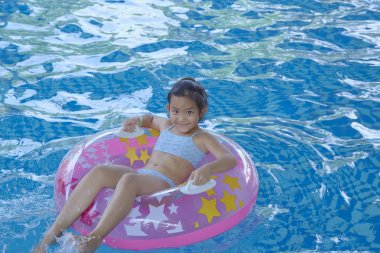 Asya Kız (9-10) yüzme havuzunda pembe şişme halka üzerinde oturan, yaz tatili kavramı