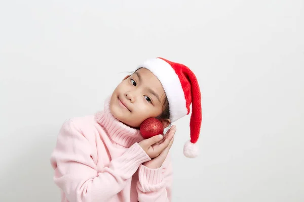 Fille tenant une boule de Noël rouge en pull et chapeau de Père Noël — Photo