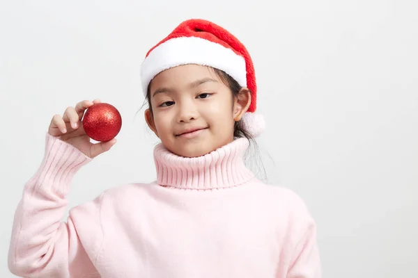 Fille tenant une boule de Noël rouge en pull et chapeau de Père Noël — Photo