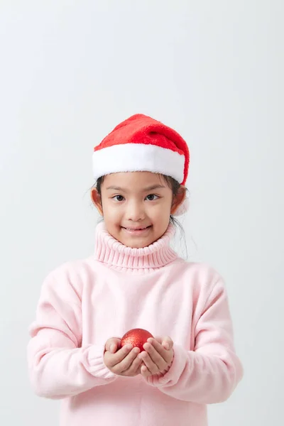 Fille tenant une boule de Noël rouge en pull et chapeau de Père Noël — Photo