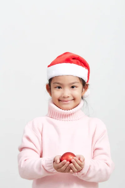 Fille tenant une boule de Noël rouge en pull et chapeau de Père Noël — Photo