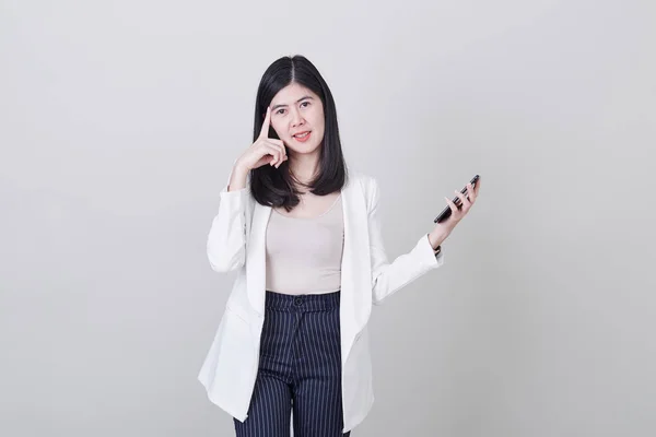 Mujer asiática pensando sosteniendo teléfono móvil —  Fotos de Stock