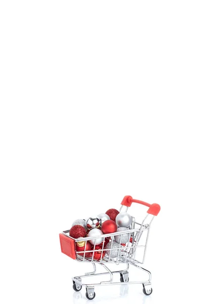 Červený vozík v supermarketu s koulemi Vánoce na bílém — Stock fotografie