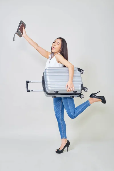 Cheerful young Asian woman with suitcase excited to travel.In the studioon Bright gray background with copy space
