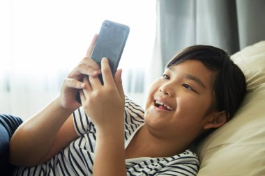 Küçük kız evdeki koltukta cep telefonu kullanmaktan hoşlanıyor..