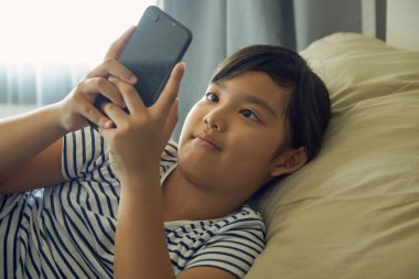 Küçük kız evdeki koltukta cep telefonu kullanmaktan hoşlanıyor..