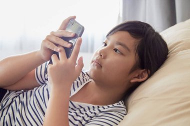 Küçük kız evdeki koltukta cep telefonu kullanmaktan hoşlanıyor..