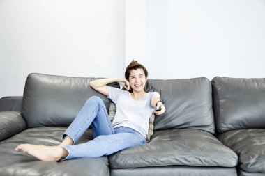 Genç Asyalı kadın evde televizyon seyrediyor ve uzaktan kumandayla kanalı değiştiriyor.