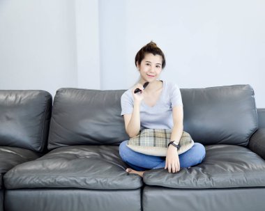 Genç Asyalı kadın evde televizyon seyrediyor ve uzaktan kumandayla kanalı değiştiriyor.