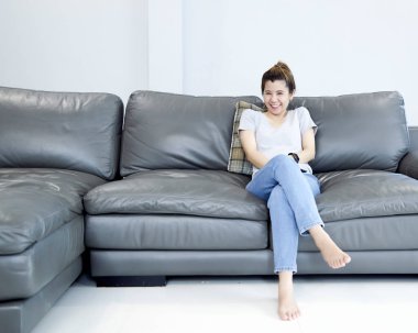 Genç Asyalı kadın evde televizyon seyrediyor ve uzaktan kumandayla kanalı değiştiriyor.