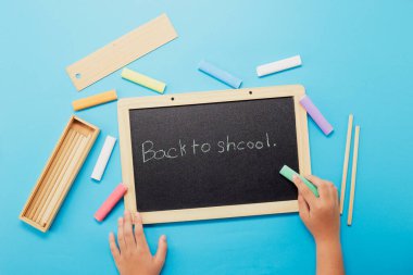 Üst el görüntüsü okula mavi arkaplanda siyah tebeşirle yazılmış.