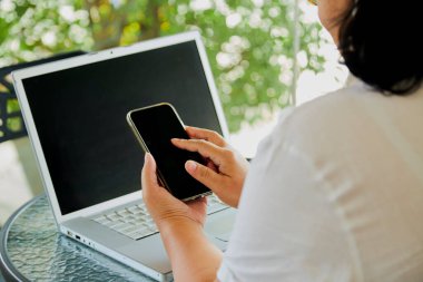 Asyalı kadın evdeki oturma odasında cep telefonu ve not defteri kullanarak oturur, resim bilgisayarı, cep telefonu boş ekranı el yazısı için çalışır, evde çalışır..