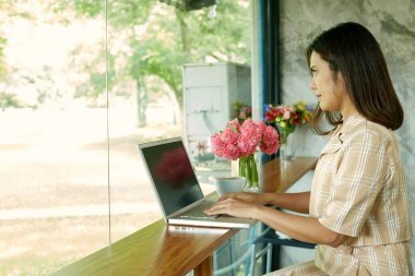 Evde dizüstü bilgisayarlı klavyeyle yazı yazan bir kadın oturuyor. Seçici odak