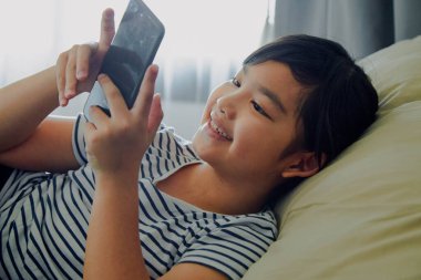 Küçük kız evde akıllı telefon kullanarak eğleniyor.