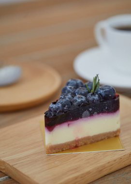 Yaban mersinli cheesecake dilimi ve ahşap masa arkasında sade kahveyle biberiye yaprağı. Lezzetli Kremalı Kek Dilimi