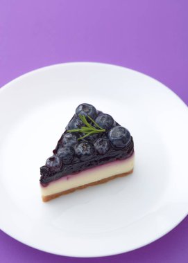 Beyaz tabakta mor arka planda yaban mersinli cheesecake.