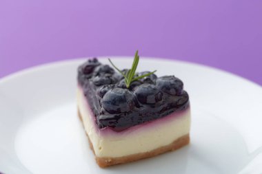 Beyaz tabakta mor arka planda yaban mersinli cheesecake.