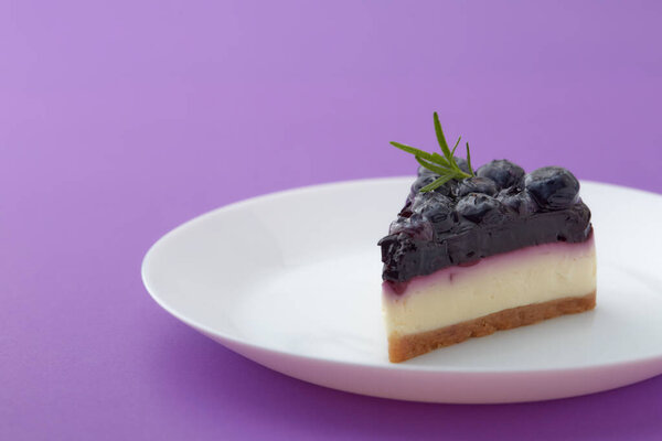 Piece of blueberry cheesecake on white plate on violet background