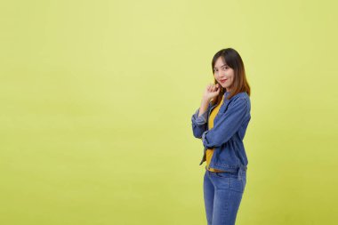 Stüdyoda sarı arka planda genç, şirin ve atletik Taylandlı bir kızın portresi. Çapraz kollu bir kadın sarı tişört, kot ceket ve basit kot pantolon giyiyor.