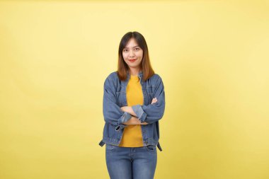 Stüdyoda sarı arka planda genç, şirin ve atletik Taylandlı bir kızın portresi. Çapraz kollu bir kadın sarı tişört, kot ceket ve basit kot pantolon giyiyor.