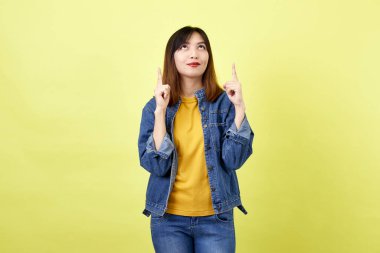 Kot ceketli mutlu Asyalı kadın fotokopi alanını gösteriyor ve sarı arkaplanda kameraya bakıyor.