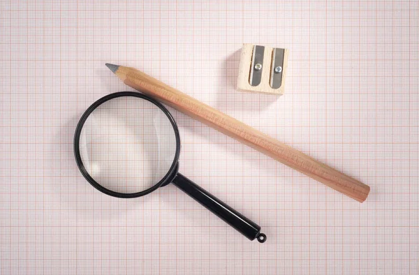 magnifying glass, pencil and sharpener over graph paper, selective focus