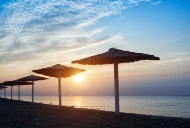 Gün batımında deniz kenarında güneşlik ve şemsiye. Tatil, yaz tatili ve seyahat için güzel bir konsept..
