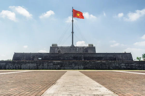 Main view of the flag of Vietnam (red flag with a gold star) fluttering over a tower of the Citadel on blue sky background in Hue, Vietnam. Within the Citadel is the Imperial City.