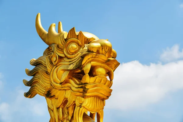 Closeup view of dragon head on blue sky background. Gilded sculpture of Asian dragon holding a pearl.