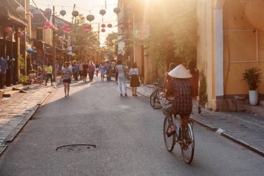 Hoi bir (Hoian), Vietnam - 11 Nisan 2018: yayalara antik şehrin görünümünü günbatımında harika. Bisiklet üzerinde geleneksel bambu şapkalı Vietnamca kadın.