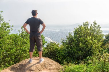 Adam harika bir manzara ve yeşil çalılar arasında dağın zirvesinde temiz hava zevk. Bir kıyı kenti arka planda görünür.