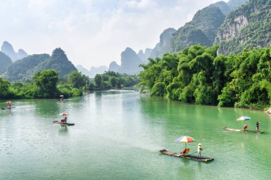 Amazing view of small tourist bamboo rafts sailing along the Yulong River among green woods and karst mountains at Yangshuo County of Guilin, China. Yangshuo is a popular tourist destination of Asia. clipart