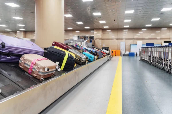 Suitcases on luggage conveyor belt and row of trolleys at arrival area of passenger terminal in airport. Baggage carousel.