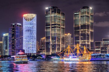Shanghai, Çin'in şehir merkezindeki Pudong Yeni alan (Lujiazui) modern waterfront binalara güzel gece manzarası. Huangpu Nehri geçerken turist tekne. Suya yansıyan renkli şehir ışıkları.