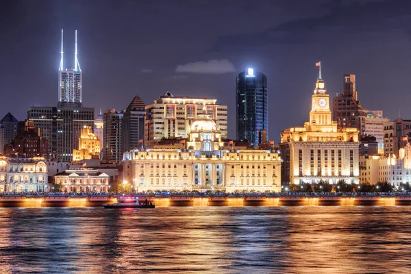 Wonderful night view of Puxi skyline in Shanghai, China. Modern and old buildings of the Bund (Waitan) at historic center. Colorful city lights reflected in water of the Huangpu River.