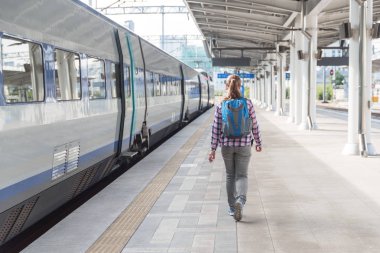 Tren yakalamak için platform yürüyen genç kadın. Kadın turist tren istasyonunda mavi sırt çantası ile. Demiryolu seyahat. Modern yüksek hızlı tren.