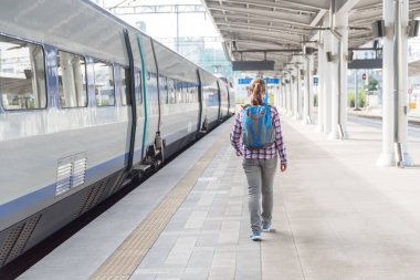 Kadın turist yürüme tren yakalamak için. Tren istasyonunda mavi sırt çantası olan kadın. Demiryolu seyahat. Modern yüksek hızlı tren.